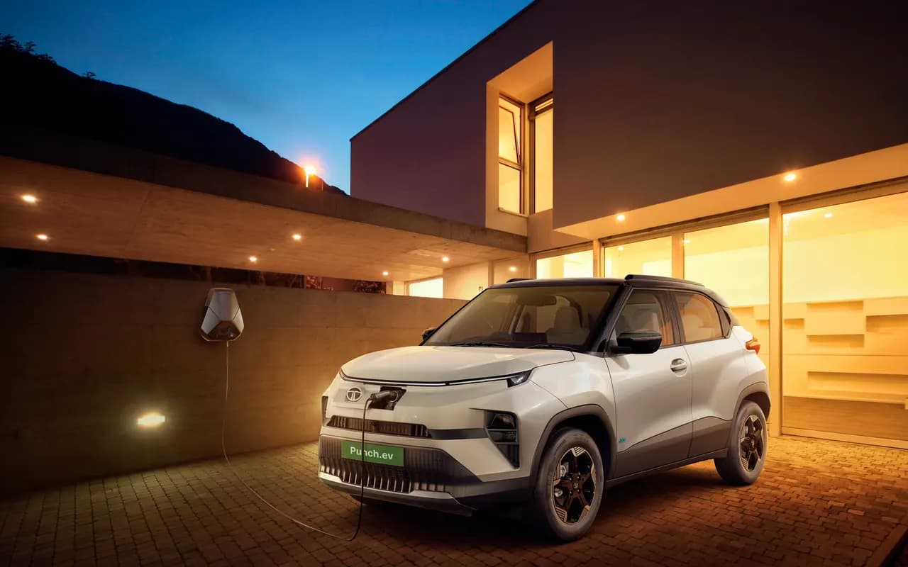 A Tata Punch.ev charging from a wall box outside a house at dusk