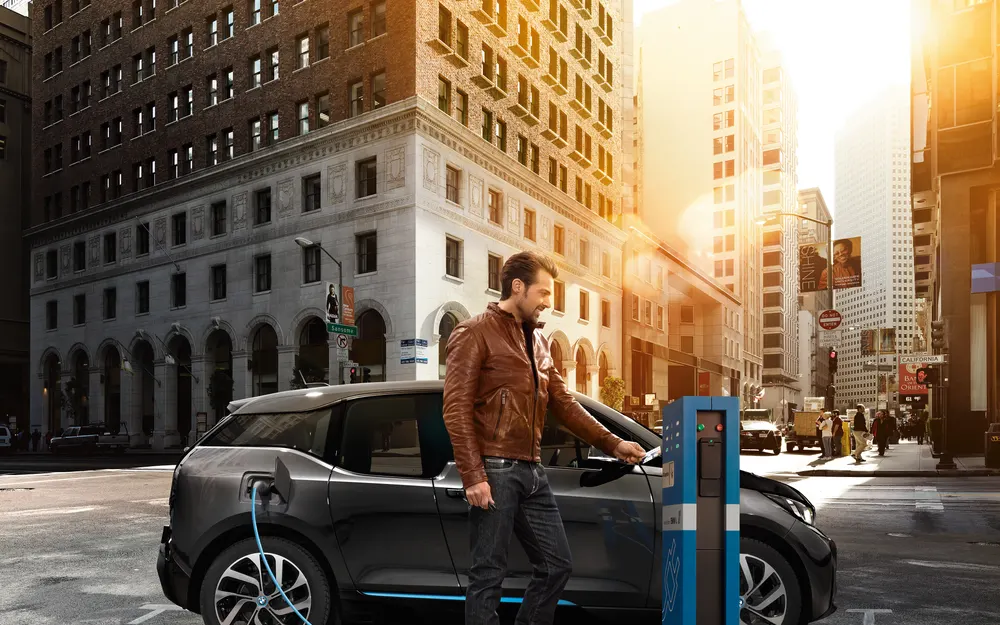 Driver plugging an electric car into a public charging post on a city street